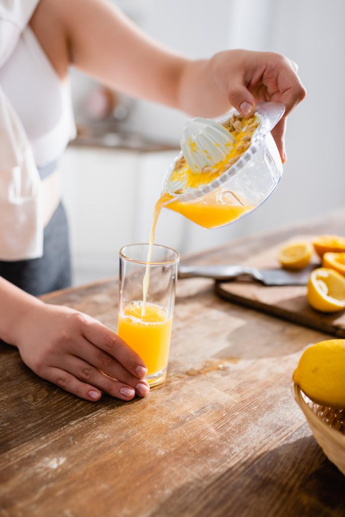 обрезанный вид женщины, наливающей свежий апельсиновый сок в стакан рядом с сжатыми фруктами  - Фото, изображение