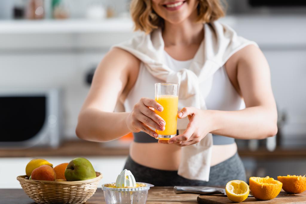 oříznutý pohled na ženu držící sklo s čerstvou pomerančovou šťávou v blízkosti vymačkaného ovoce - Fotografie, Obrázek