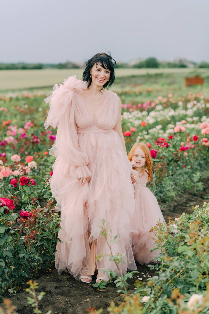 Μαμά και κόρη με ροζ φορέματα σε ένα λιβάδι με τριαντάφυλλα - Φωτογραφία, εικόνα