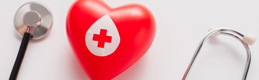 bovenaanzicht van rood hart en stethoscoop op wit, bloeddonatie concept - Foto, afbeelding