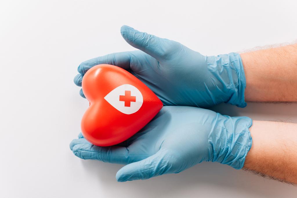 vista recortada de las manos masculinas en guantes de látex con corazón rojo sobre blanco, concepto de donación de sangre - Foto, Imagen