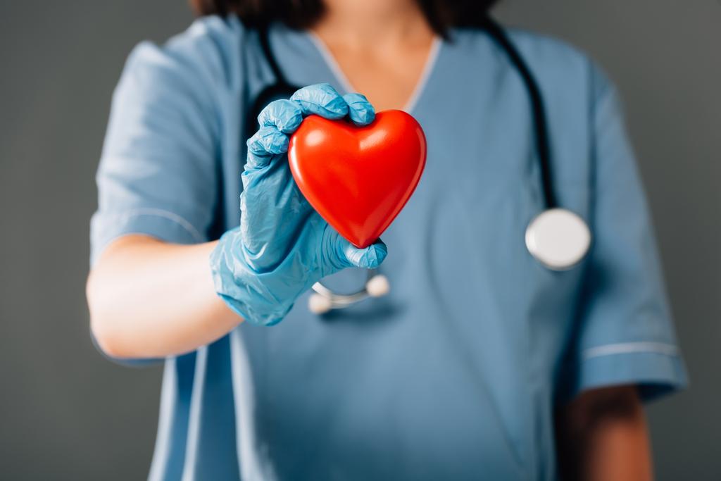 灰色に隔離された赤い心臓を保持するラテックス手袋の立体視を持つ医師のクロップドビュー - 写真・画像