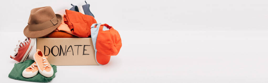 panoramatický záběr lepenkové krabice s darovaným příslušenstvím, oblečením a obuví izolovanou na bílém, charitativní koncept - Fotografie, Obrázek