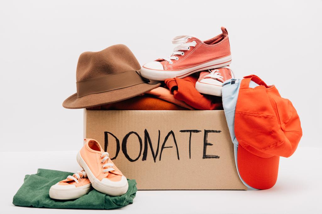 caja de cartón con accesorios donados, ropa y calzado aislado en blanco, concepto de caridad - Foto, Imagen