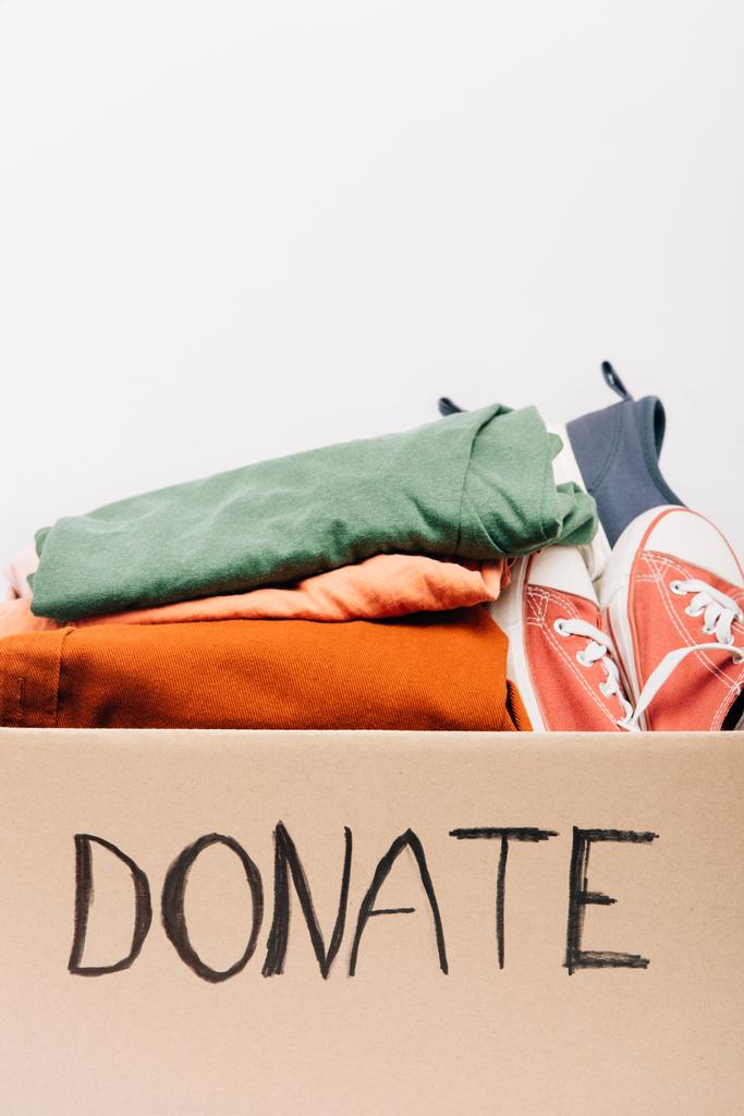 boîte en carton avec des vêtements donnés et des chaussures isolées sur blanc, concept de charité - Photo, image