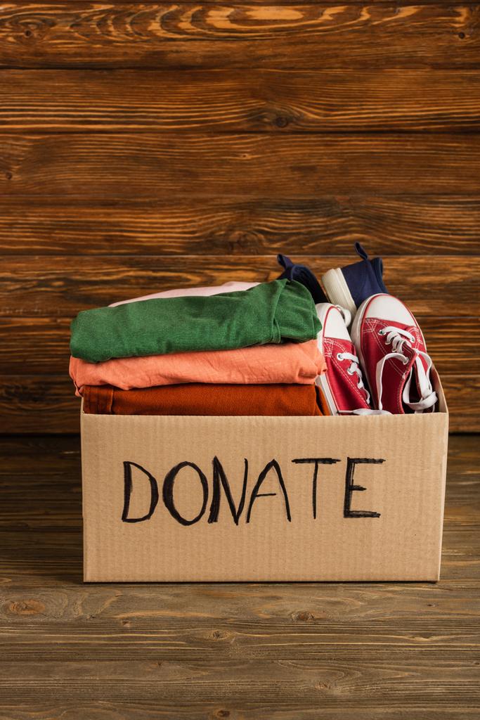 caixa de papelão com roupas doadas e calçados em fundo de madeira, conceito de caridade
 - Foto, Imagem