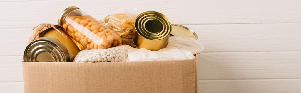 Panoramaaufnahme eines Kartons mit gespendeten Lebensmitteln auf Holzgrund, Charity-Konzept - Foto, Bild