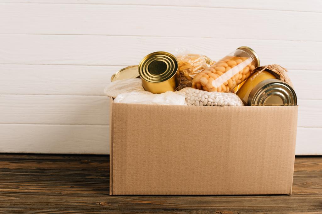 scatola di cartone con cibo donato su sfondo di legno, concetto di carità - Foto, immagini