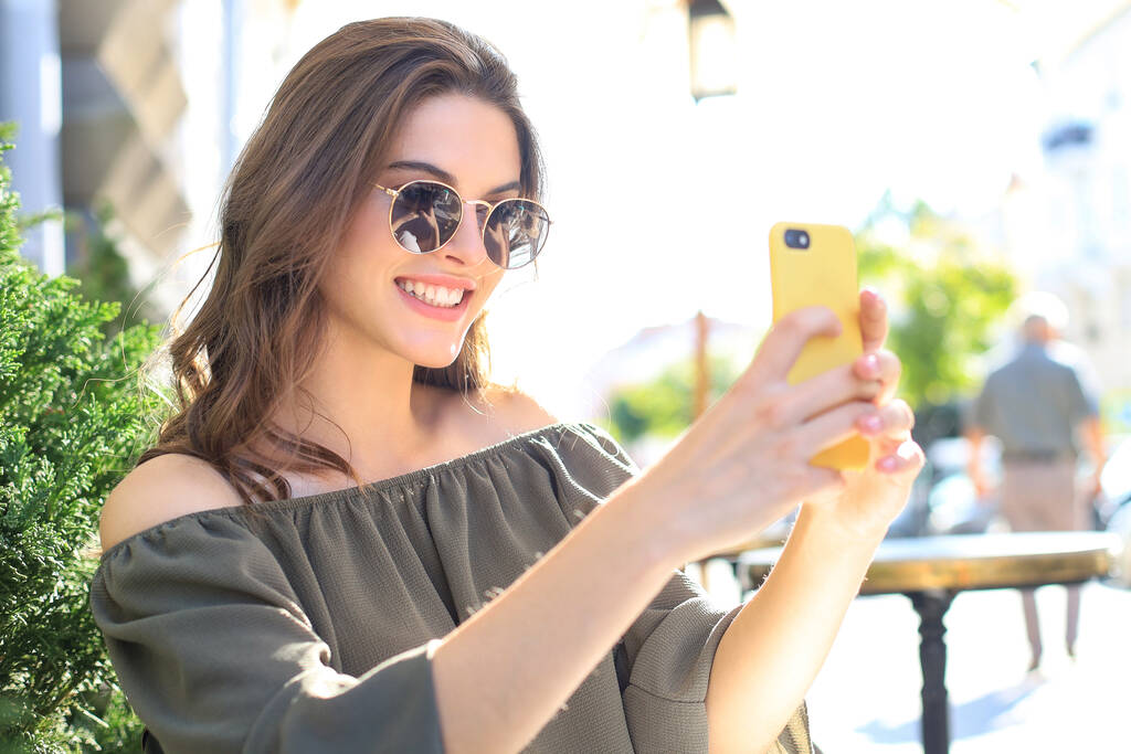 Νεαρή όμορφη μελαχρινή γυναίκα σε εξωτερικούς χώρους το καλοκαίρι στην πόλη να πάρετε μια selfie από το κινητό τηλέφωνο - Φωτογραφία, εικόνα
