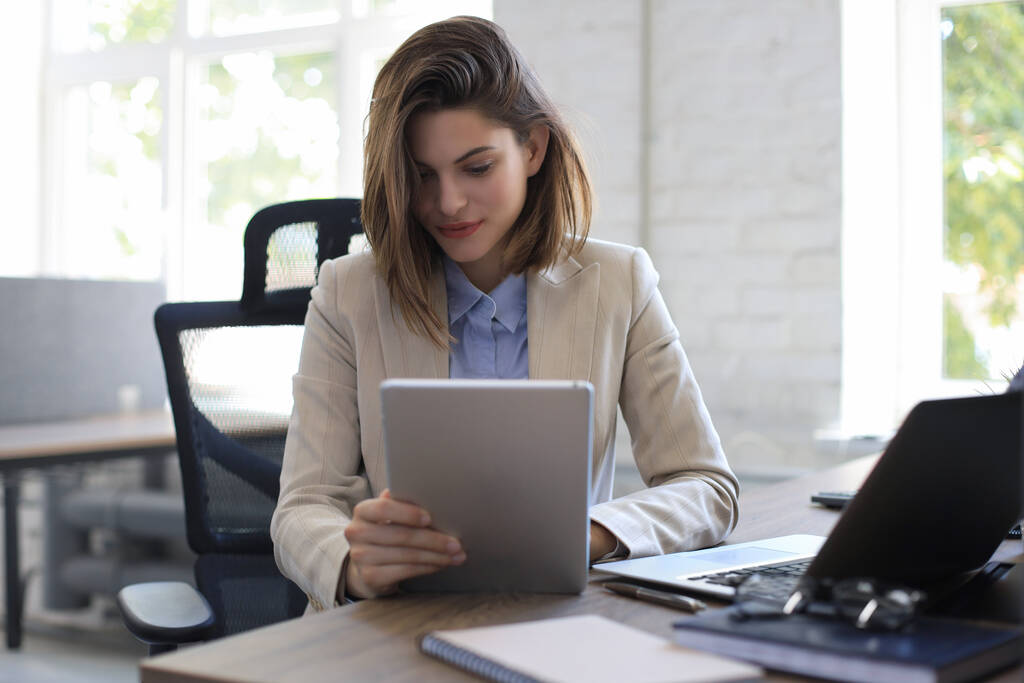 Aantrekkelijke glimlachende vrouw aan het werk op een tablet in modern kantoor - Foto, afbeelding