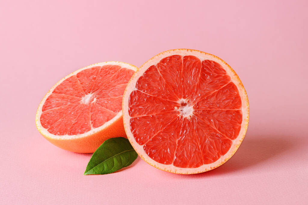Dvě poloviny čerstvě zralého šťavnatého grapefruitu a listí na růžovém pozadí. Vegetariánská, syrová strava a zdravé stravování. Organický antioxidant. Pohled zepředu. - Fotografie, Obrázek