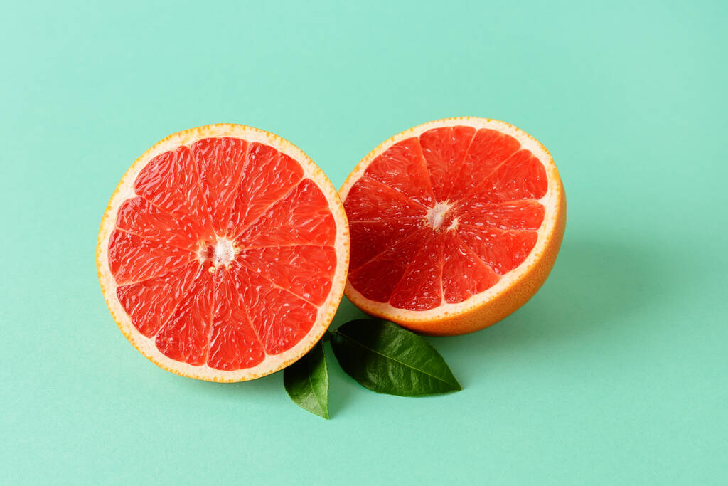Twee helften vers rijp sappig grapefruit en twee bladeren op een muntgroene achtergrond. Vegetarisch, rauw voedsel dieet en gezond eten. Organische antioxidant. Vooraanzicht. - Foto, afbeelding