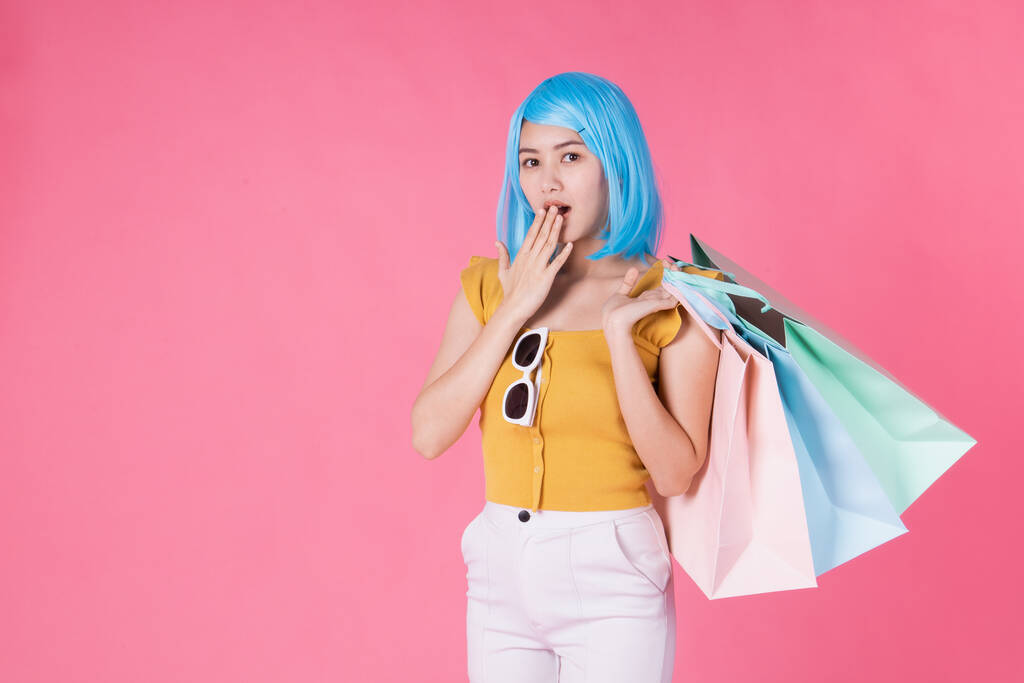Πορτρέτο ενός αρκετά ενθουσιασμένος ασιατικό κορίτσι με πολύχρωμες τσάντες ψώνια δείχνει απομονωμένη σε ροζ φόντο.Ασιατική shopaholic γυναίκα μεταφέρουν τσάντες ψώνια σε πολύχρωμα για την έννοια της καλοκαιρινής πώλησης .νεαρό κορίτσι μπλε μαλλιά . - Φωτογραφία, εικόνα