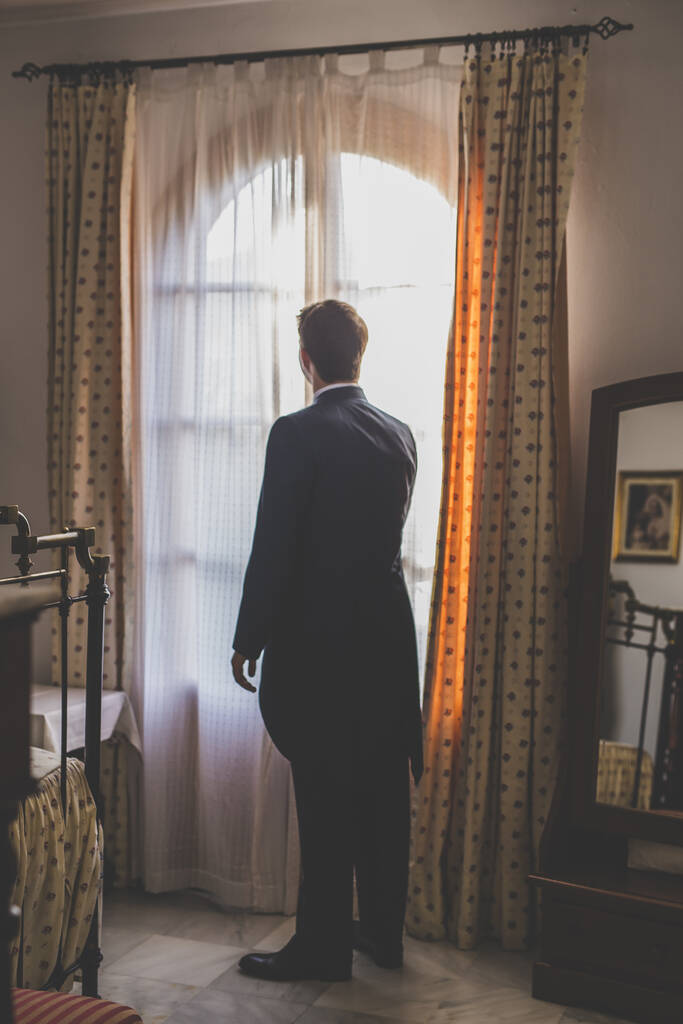 Вертикальный снимок молодого мужчины в костюме, смотрящего в окно - Фото, изображение