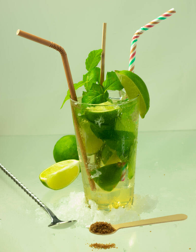 Um tiro vertical de um coquetel de mojito com rum, limão e folhas de hortelã em uma superfície verde clara
 - Foto, Imagem