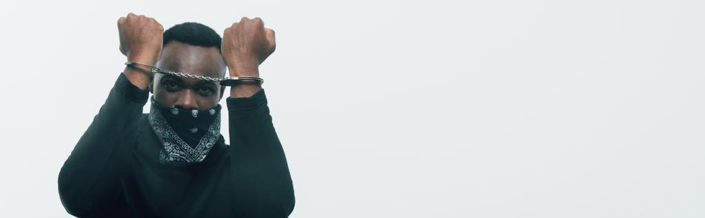 tiro panorâmico de homem afro-americano algemado olhando para câmera isolada em branco, conceito de racismo
  - Foto, Imagem