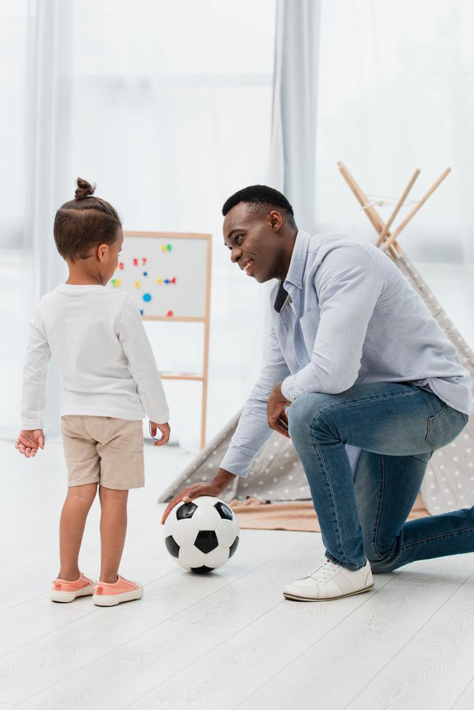 Afrikanisch-amerikanischer Vater rührt Fußball an und schaut Kind an  - Foto, Bild