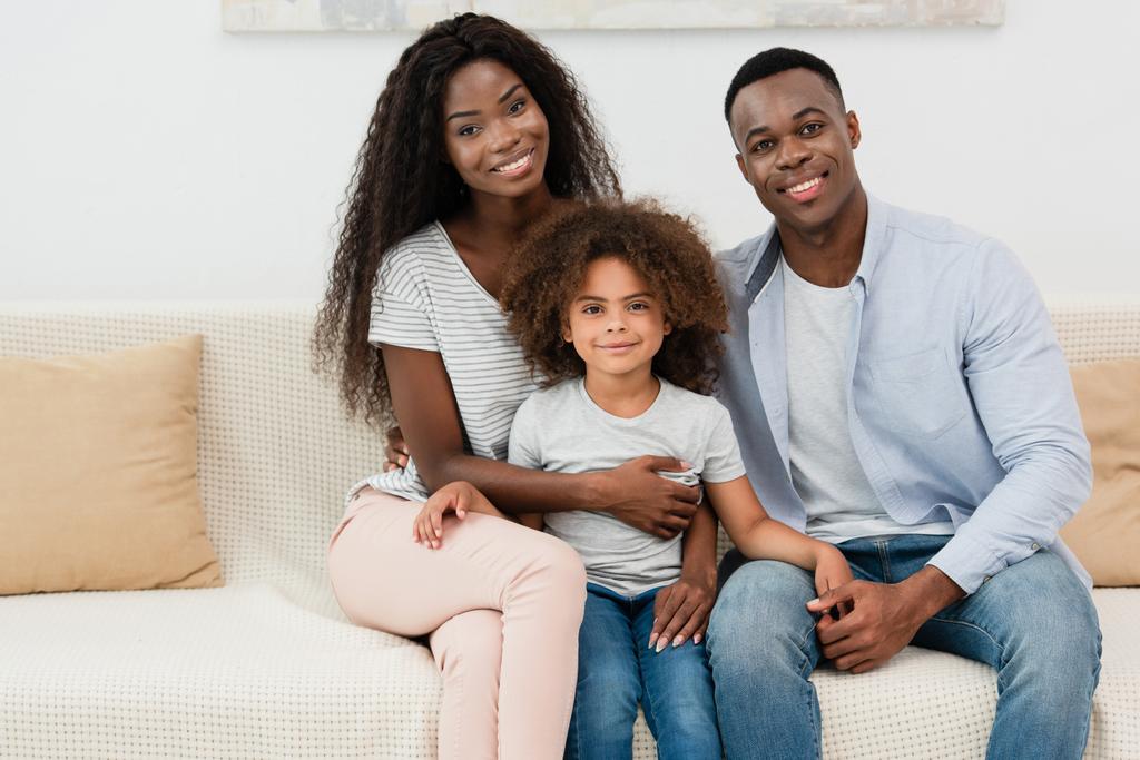 familia afroamericana mirando a la cámara y sentado en el sofá en la sala de estar  - Foto, Imagen