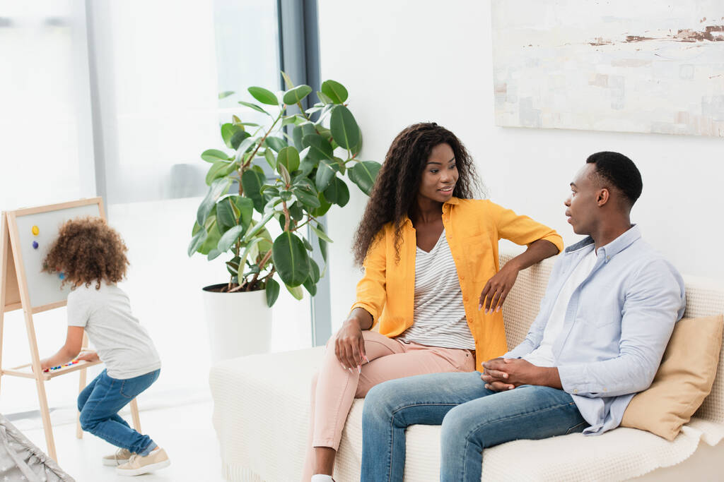 アフリカ系アメリカ人の両親がソファに座り磁気イーゼルの近くに立つ娘が - 写真・画像