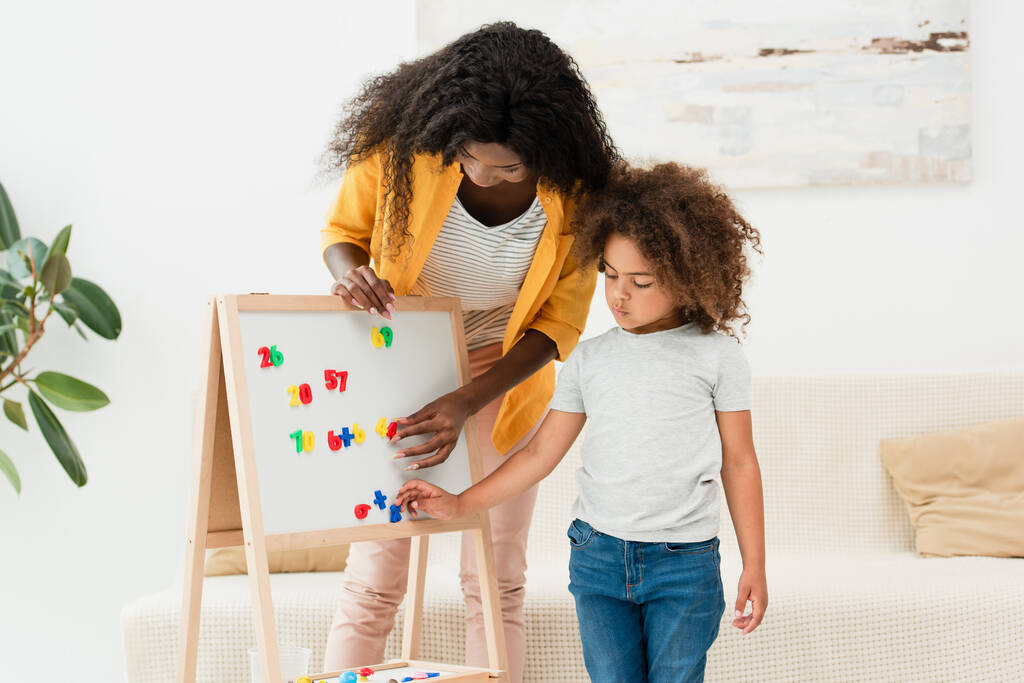 Afrikaans-Amerikaanse moeder en dochter aanraken magneten op whiteboard  - Foto, afbeelding