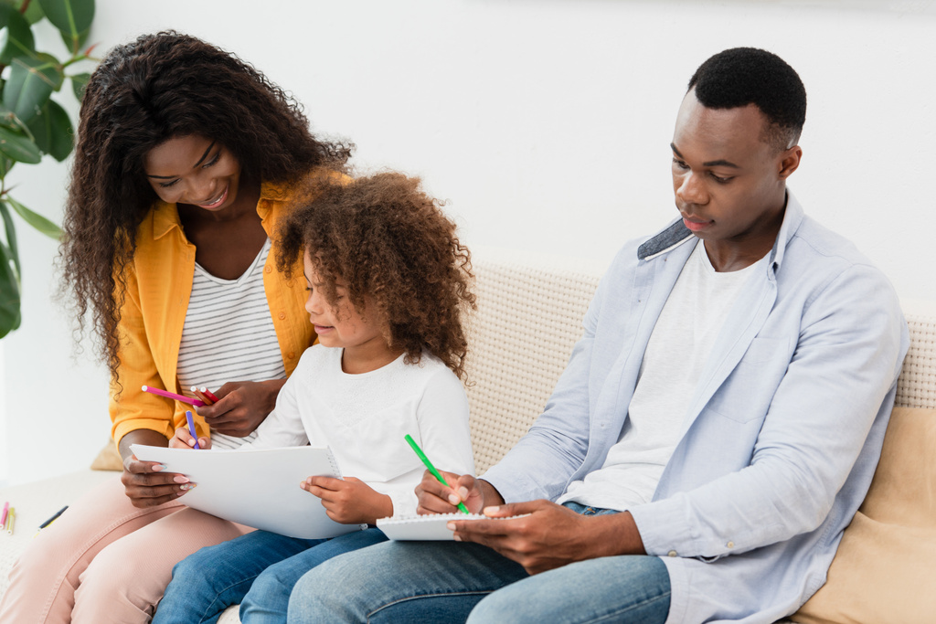 Afrikaans-Amerikaanse familie tekening met kleurpotloden terwijl zitten op de bank  - Foto, afbeelding