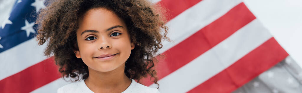 cultivo panorámico de niño rizado afroamericano mirando la cámara cerca de la bandera de América - Foto, imagen