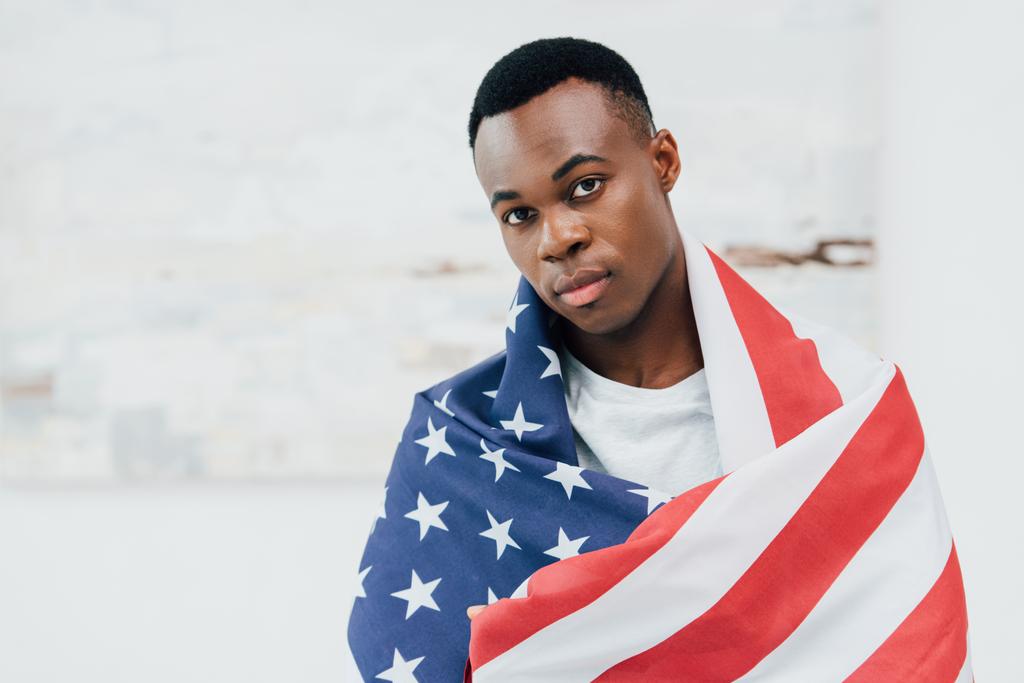 africký Američan muž pokrytý vlajkou amerického pohledu na kameru - Fotografie, Obrázek