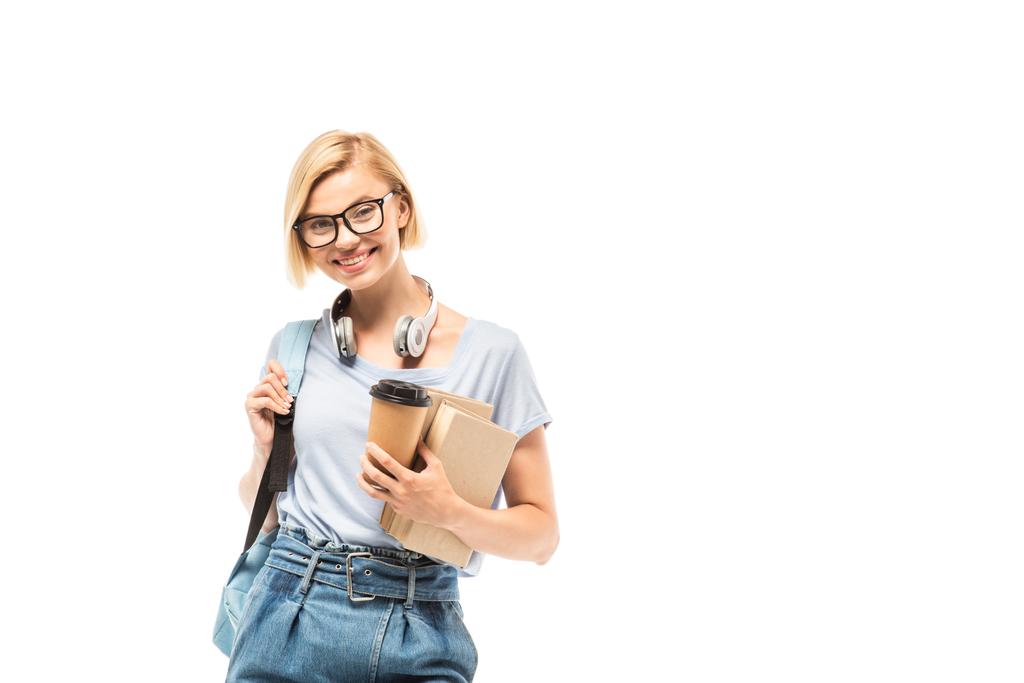 Estudiante con mochila mirando a la cámara mientras sostiene el café para llevar y libros aislados en blanco - Foto, Imagen
