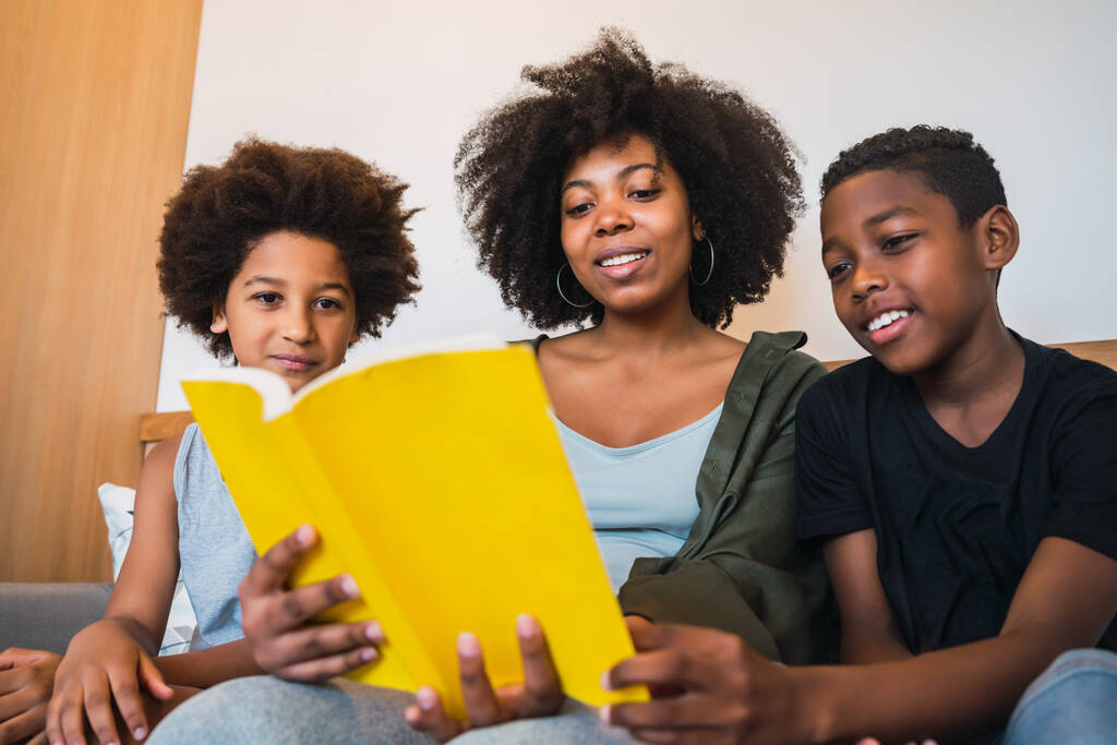 Portrait of Afro American mother reading a book to her children at home. Family and lifestyle concept. - Photo, Image