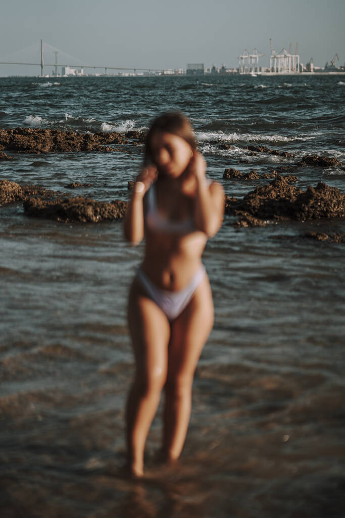 Egy függőleges homályos kép egy szexi nő bikiniben pózol a háttérben a tenger - Fotó, kép