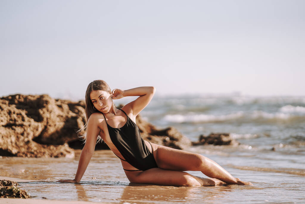 ビーチの砂の上に座っている水着のセクシーな女性 - 写真・画像