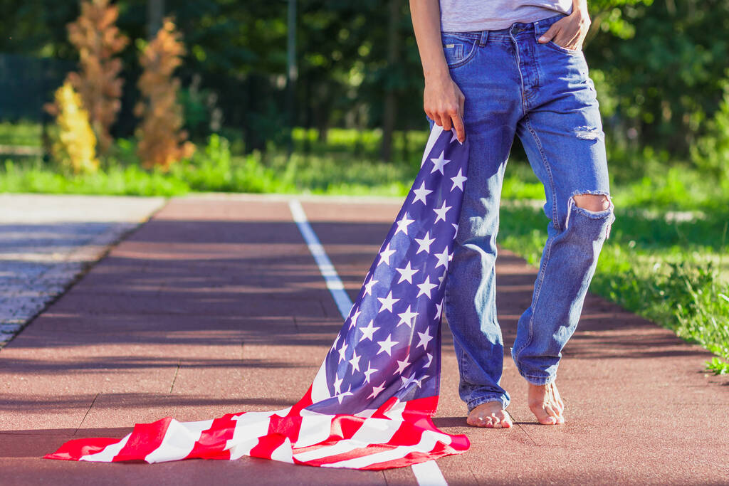 Femme avec un drapeau des États-Unis d'Amérique dans les mains, à l'extérieur, fond de mise au point doux - Photo, image