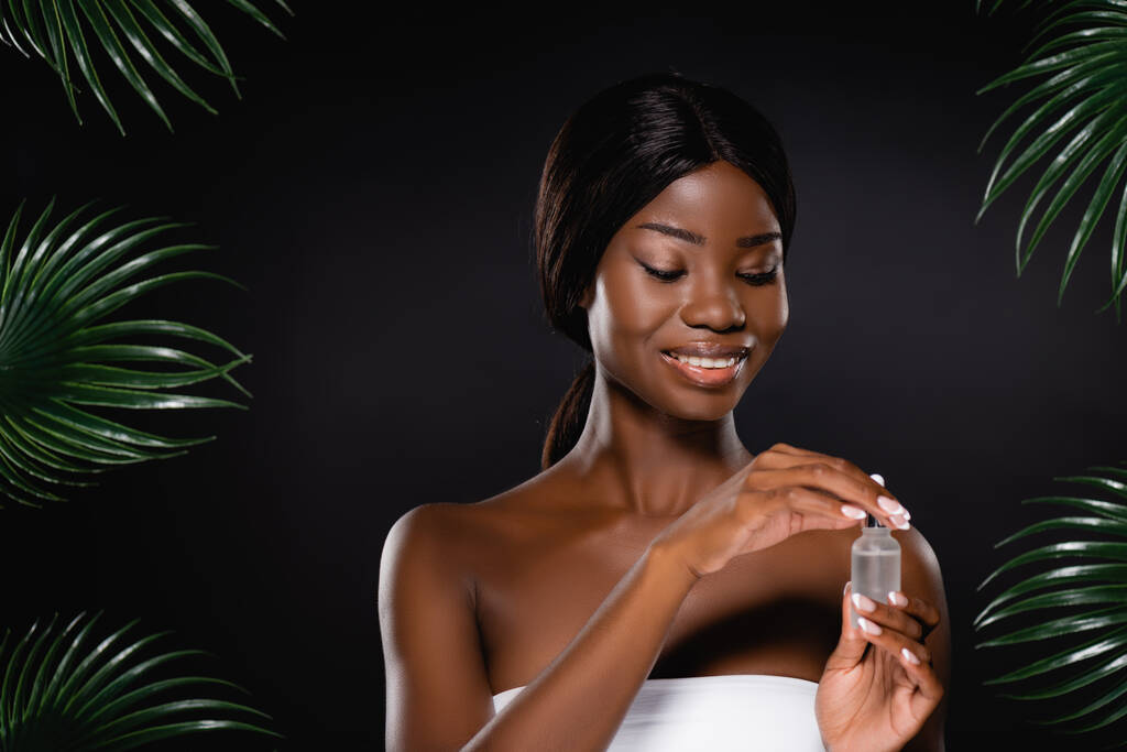 Siyah palmiye yapraklarının yanında serumla şişe tutan Afro-Amerikan kadın. - Fotoğraf, Görsel