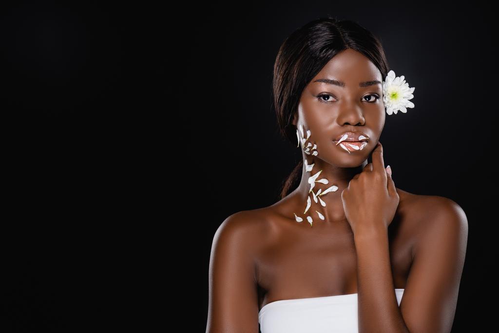 african american woman with white chrysanthemum in hair and petals on neck and lips isolated on black - Photo, Image