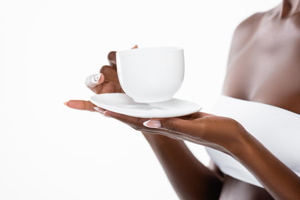 καλλιεργημένη άποψη της αφρικανικής αμερικανικής γυναίκας με φλιτζάνι καφέ και πιατάκι απομονώνονται σε λευκό - Φωτογραφία, εικόνα