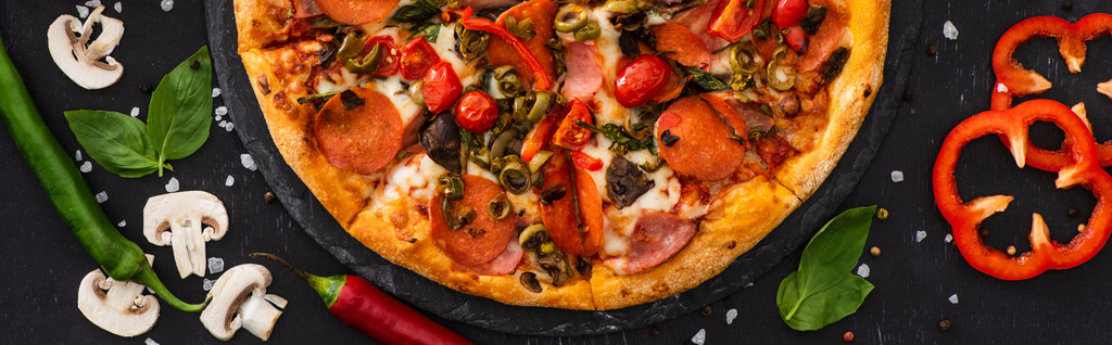 Draufsicht auf köstliche italienische Pizza mit Gemüse und Salami auf schwarzem Hintergrund, Panoramaaufnahme - Foto, Bild