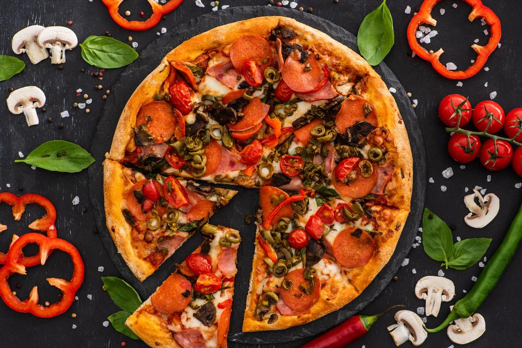 vista superior de la deliciosa pizza italiana con verduras y salami sobre fondo negro - Foto, imagen