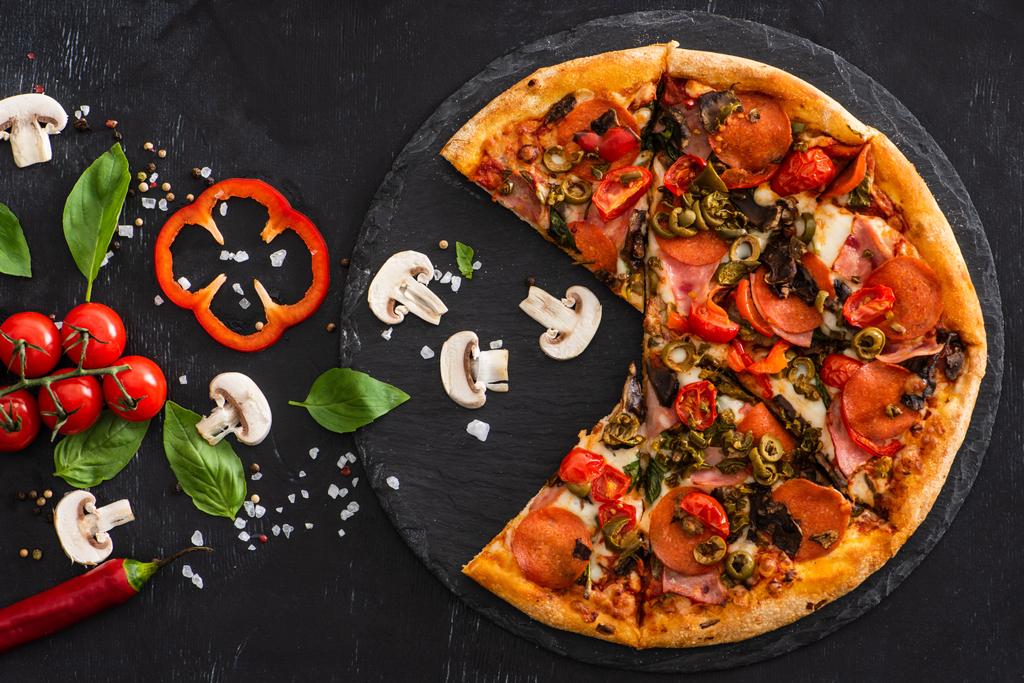 vista superior de deliciosa pizza italiana com legumes e salame no fundo preto
 - Foto, Imagem