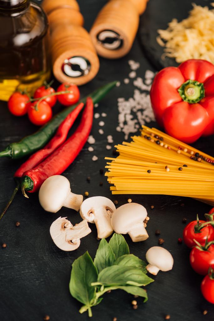selective focus of raw Italian spaghetti with vegetables on black background - Photo, Image