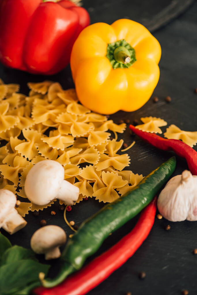 raw Italian farfalle with vegetables on black background - Photo, Image