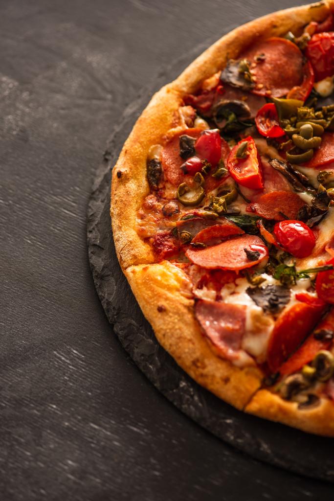 vue du dessus de délicieuse pizza italienne avec légumes et salami sur fond de bois noir - Photo, image