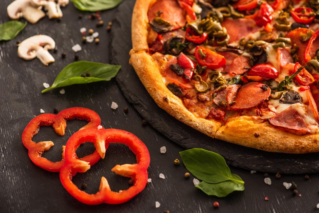 close up view of delicious Italian pizza with salami near vegetables on black background - Photo, Image
