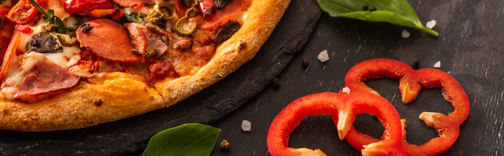 vista de cerca de la deliciosa pizza italiana con salami cerca de verduras sobre fondo negro, plano panorámico - Foto, Imagen