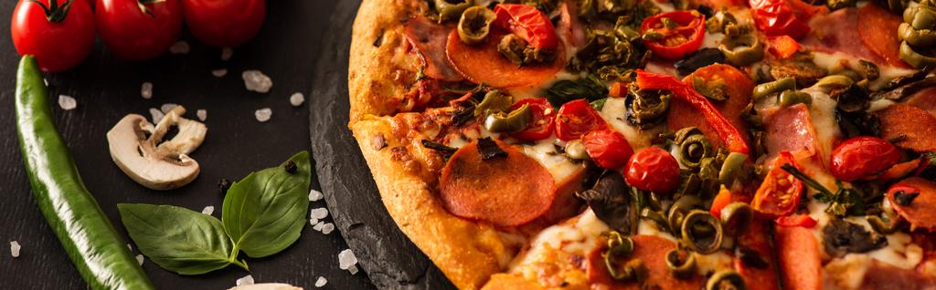 heerlijke Italiaanse pizza met salami in de buurt van groenten op zwarte achtergrond, panoramische shot - Foto, afbeelding