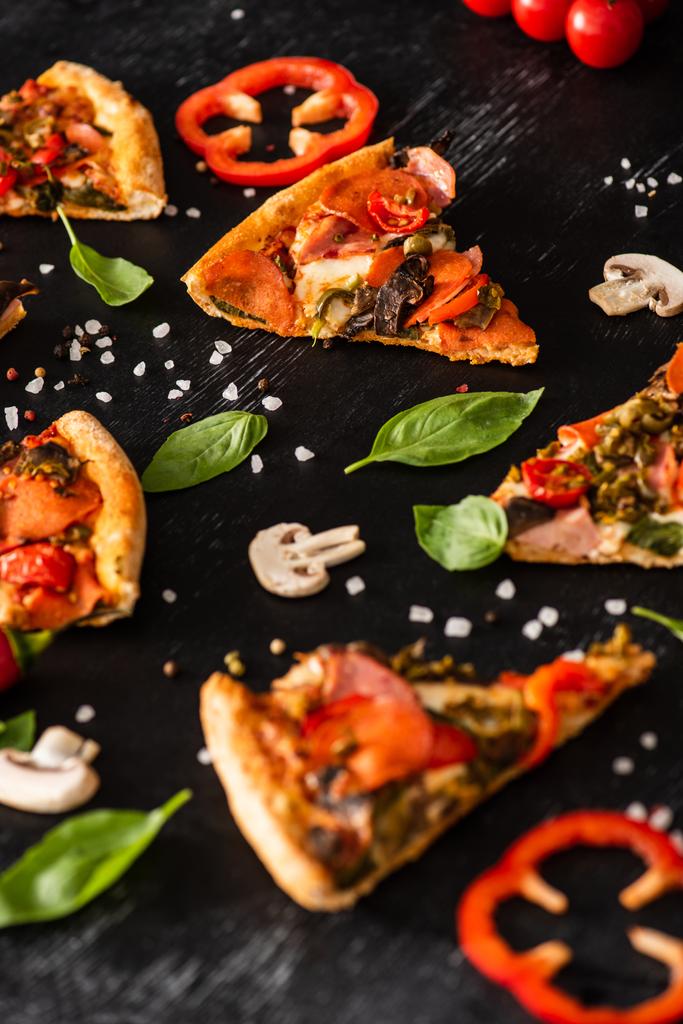 Вибіркове фокусування смачних італійських шматочків піци з салямі біля овочів на чорному тлі - Фото, зображення