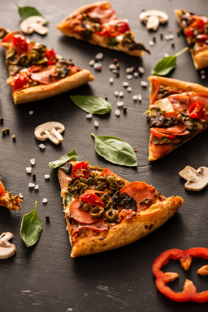 selectieve focus van heerlijke Italiaanse pizza plakjes met salami in de buurt van groenten op zwarte achtergrond - Foto, afbeelding
