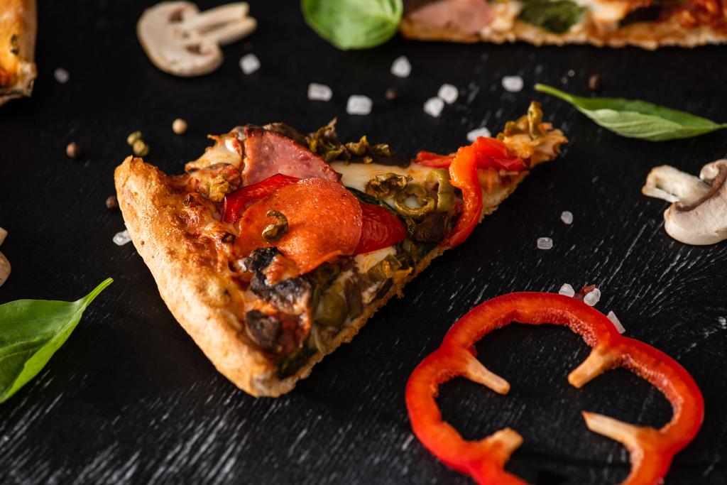 pyszne włoski kawałek pizzy z salami w pobliżu warzyw na czarnym tle - Zdjęcie, obraz