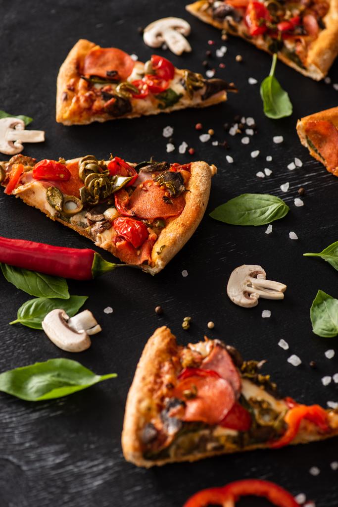 enfoque selectivo de deliciosas rebanadas de pizza italiana con salami cerca de verduras sobre fondo negro - Foto, imagen