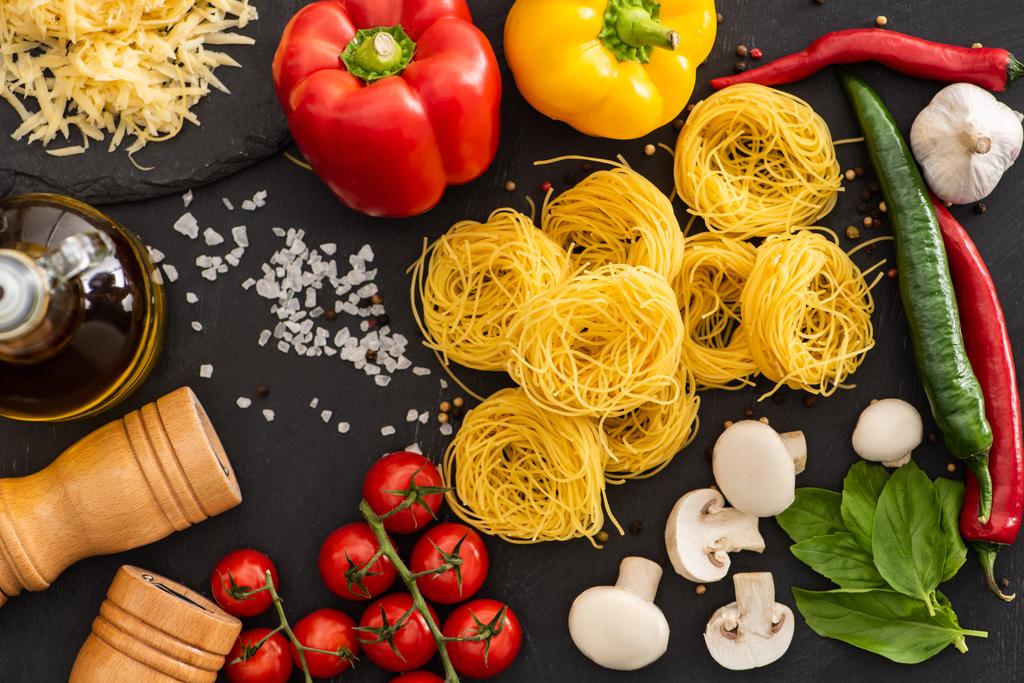 vista superior de Capellini italiano crudo con verduras y condimentos sobre fondo negro - Foto, imagen