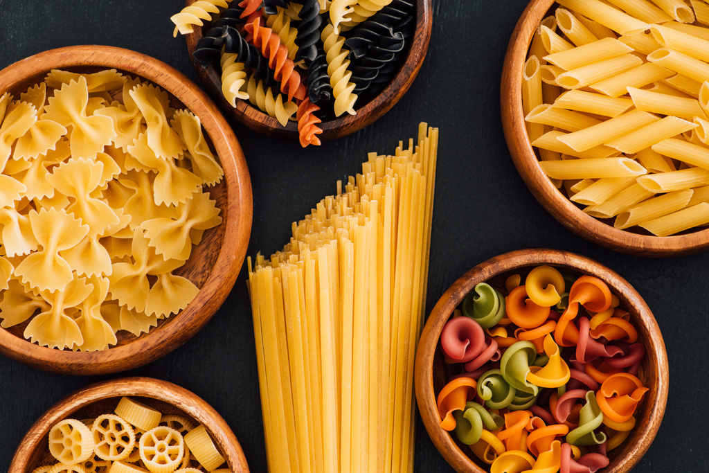 top view of assorted colorful Italian pasta in wooden bowls on black background - Photo, Image